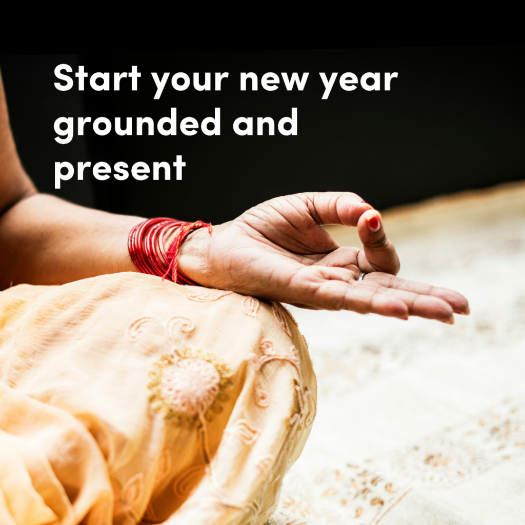 A hand resting on a knee in a sitting yoga pose with the text, 'Start your new year grounded and present.'