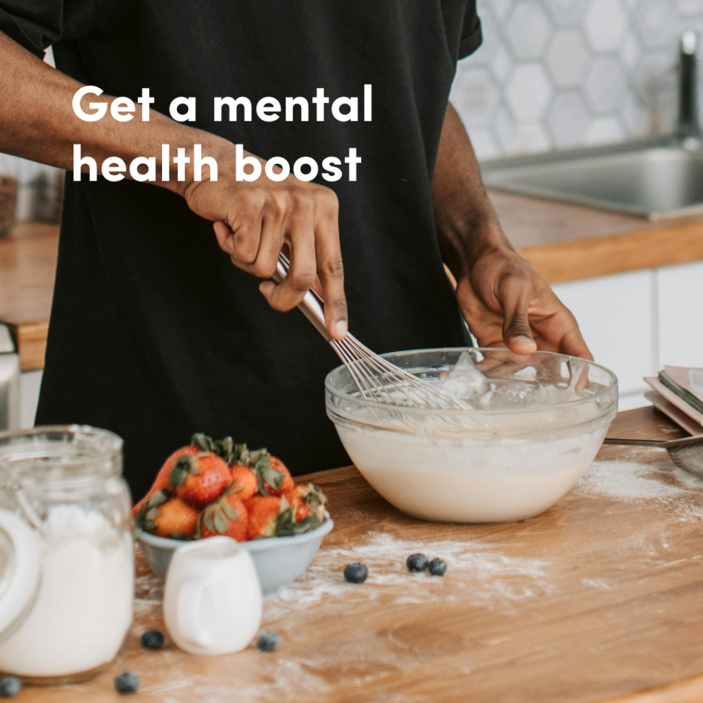 A person in a black shirt mixing a bowl on a table with flour and a bowl of strawberries with the text, 'Get a mental health boost.'